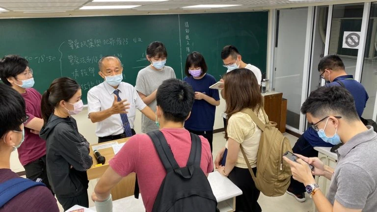警大研究所好考嗎?在職輪班怎麼準備、上榜心得與免費申論批改 2 老師在教室黑板前與圍在桌旁的學員交流